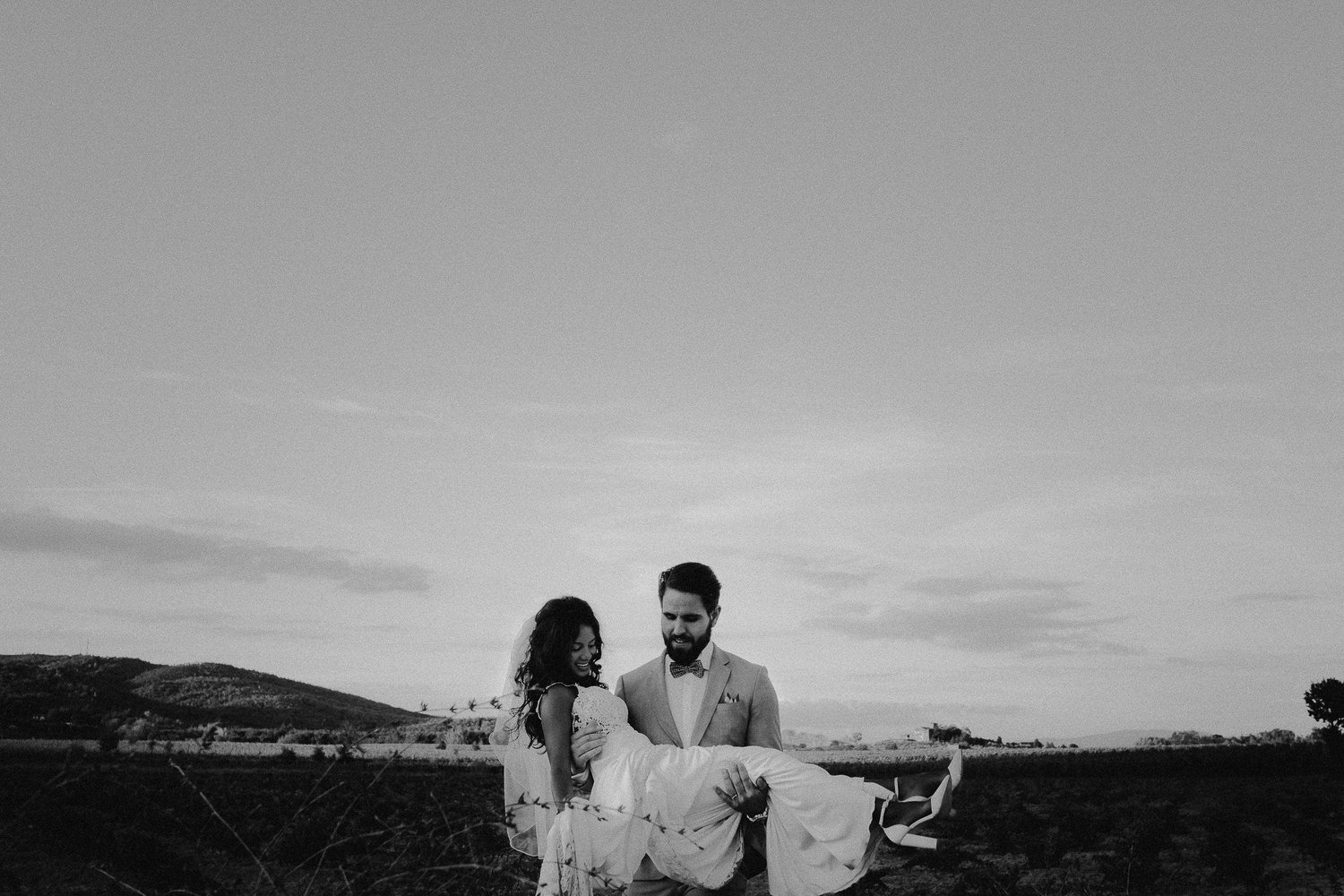 bride groom carrying bride across wine field in tuscany by mark hadden amsterdam wedding photographer