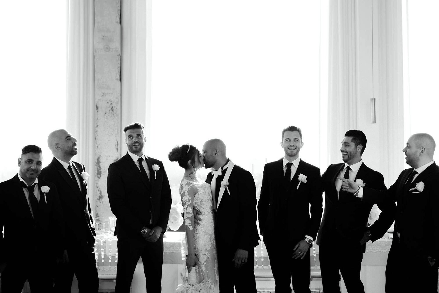 Kareline_Amir_258_2 - Bride and groom kissing while groomsmen watch in amsterdam loft wedding photoshoot.jpg