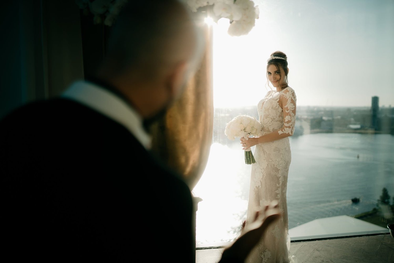 Kareline_Amir_289 - Bride holding bouquet posing in amsterdam loft with groom out of focus in foreground.jpg